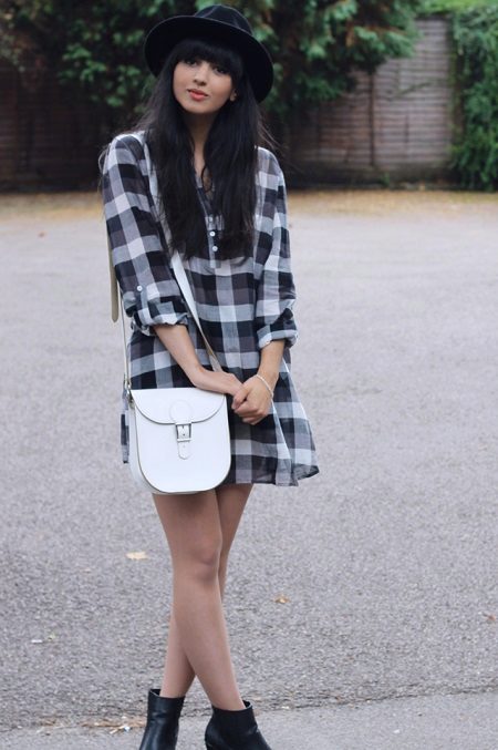 A check shirt dress in combination with a white handbag with a long strap, black boots and a hat